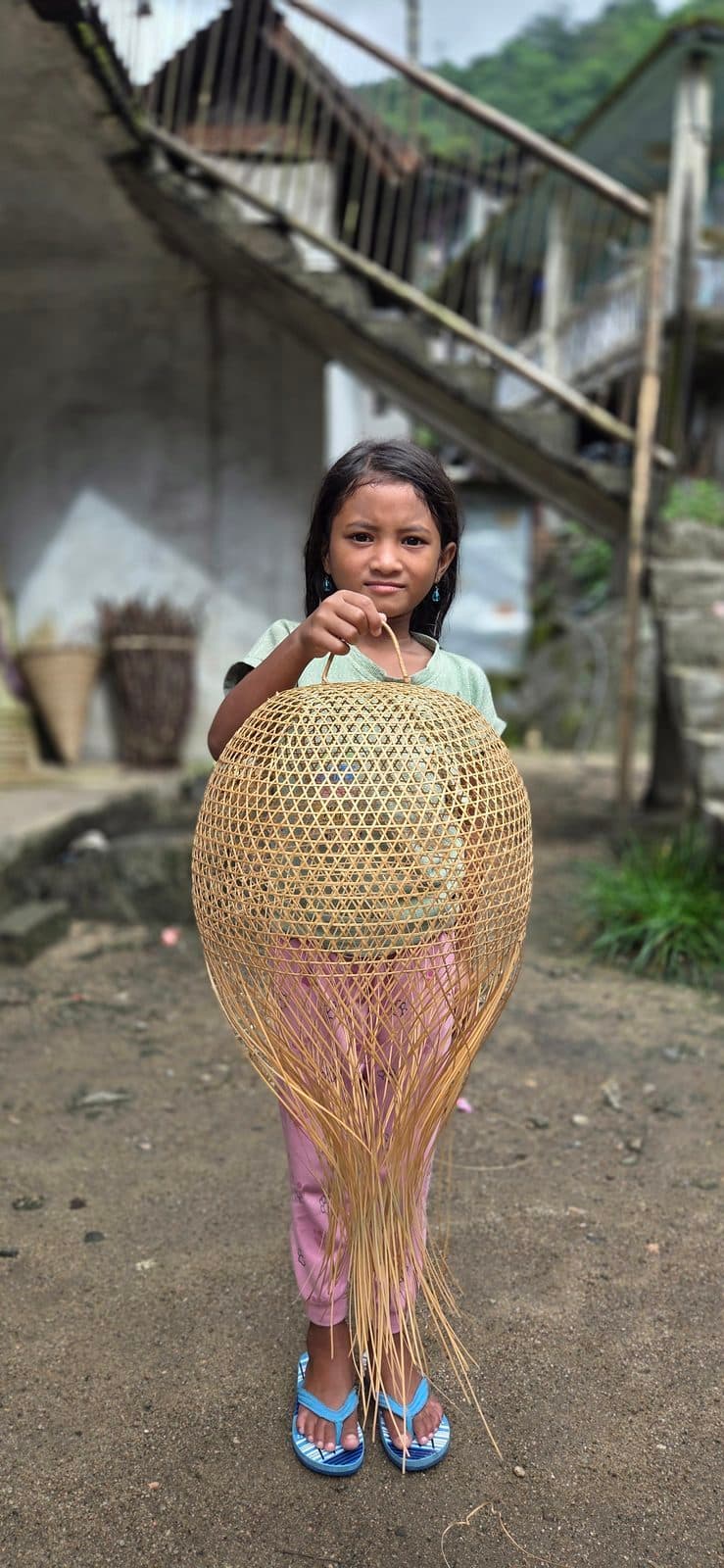 Globe bamboo pendant shade held up outside a village workshop, showing its size